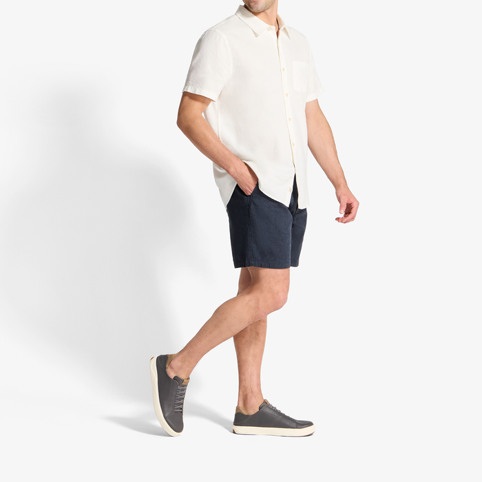 Man wearing cream short-sleeve button-up shirt and dark navy shorts with gray slip-on sneakers.