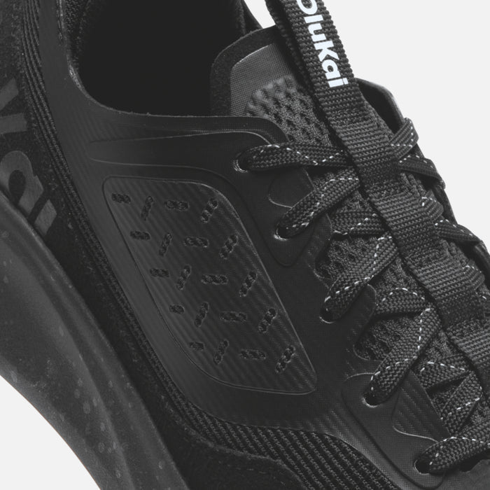 Black lace-up athletic shoe with mesh and rubber panels, featuring textured sole and brand webbing strap.