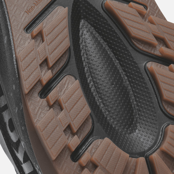 Black shoe sole with brown textured tread pattern and grip dots visible from underside view.