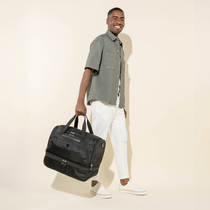 lifestyle view of a man carrying the black travelpro maxlite 5 drop bottom weekender by the bale handles showing the separate lower compartment.