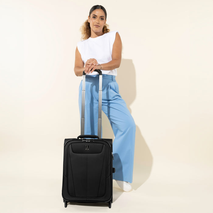 Woman standing with a Travelpro Maxlite 5 International Carry-On Rollaboard in black, hand resting on the extended handle.