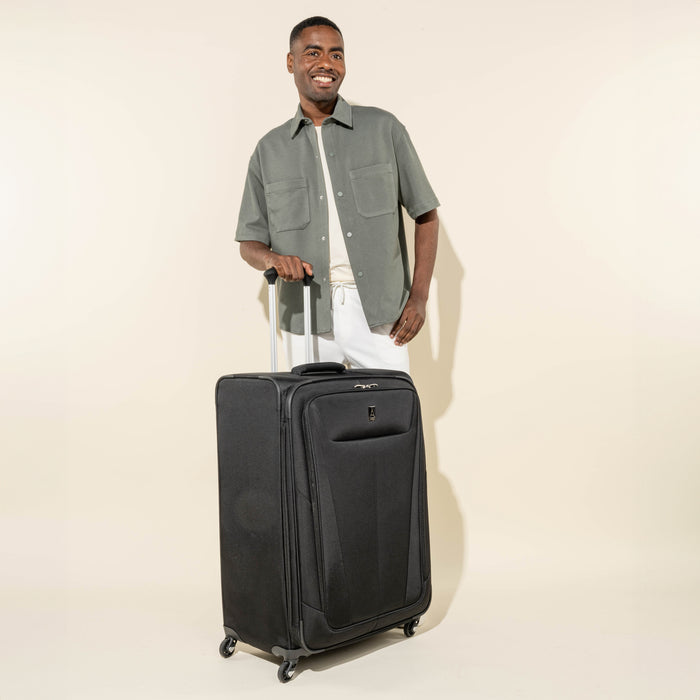 lifestyle view of a man standing next to the black travelpro maxlite 5 large check-in spinner showing the suitcase's tall profile and four 360 degree rotating spinner wheels.