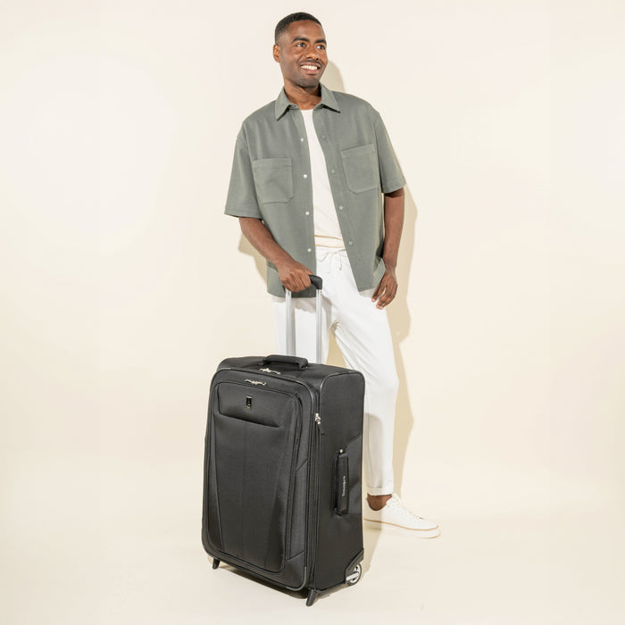 lifestyle view of a man standing with the black travelpro maxlite 5 medium check-in rollaboard suitcase, showing the bag's medium-sized capacity, extended powerscope lite handle, and high-performance wheels.