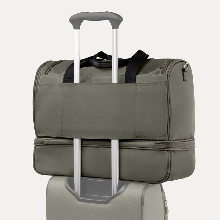 rear view of the slate green travelpro maxlite 5 drop bottom weekender showing the integrated rear strap slipped over the telescoping handle of a suitcase for secure stacking.
