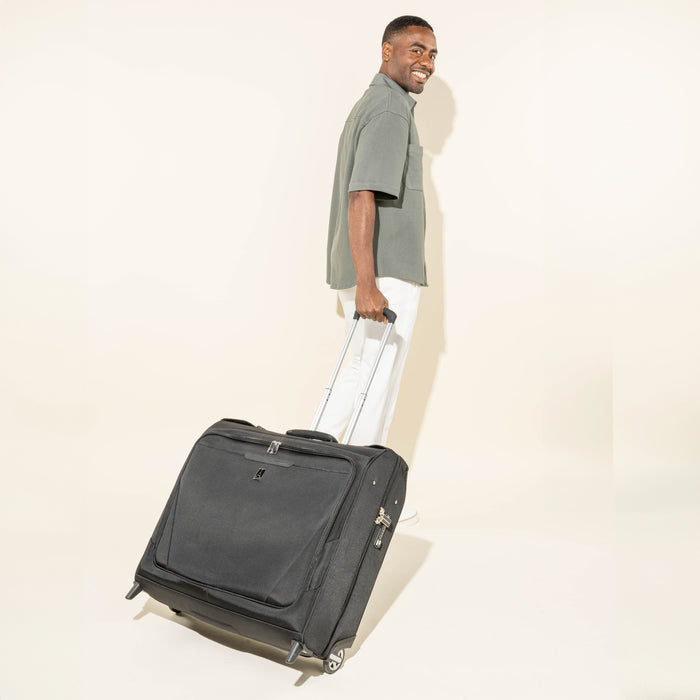 lifestyle view of a man pulling a black travelpro maxlite checked rolling garment bag by its telescoping handle.