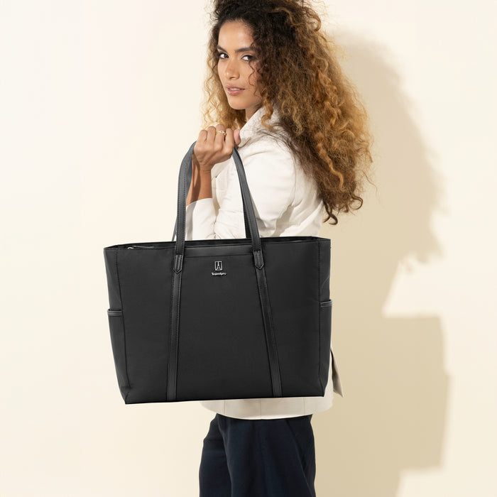 lifestyle view of a woman carrying the black travelpro maxlite women's tote over her shoulder showing the sleek bale handles and compact design.