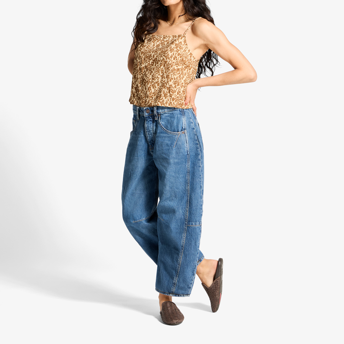 Woman wearing beige speckled sleeveless top and blue denim jeans with brown slip-on shoes.