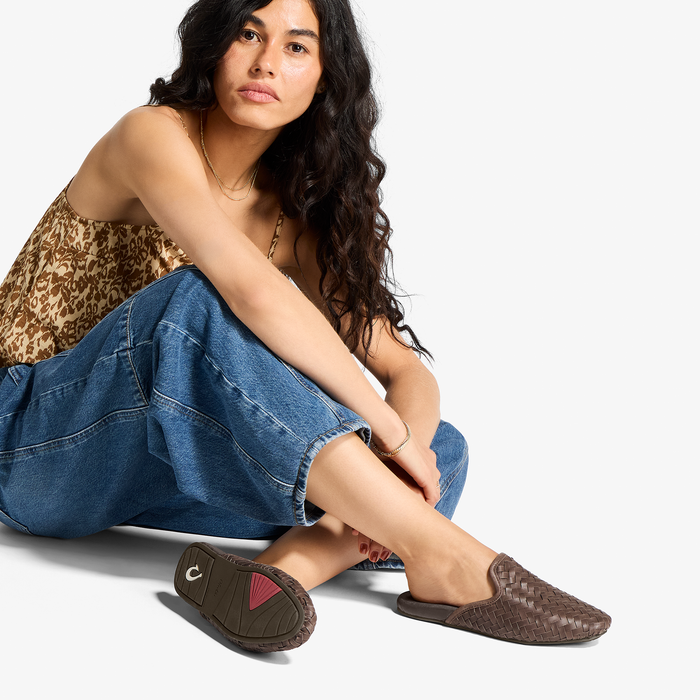 Woman wearing dark brown woven slide sandals with blue jeans and leopard print top.