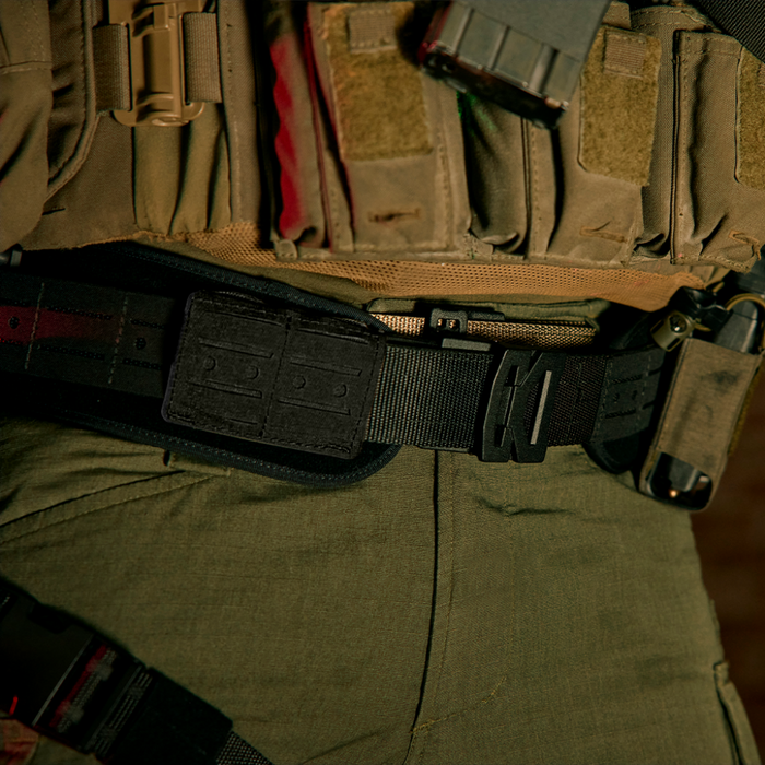 Close-up of a person wearing Kore Essentials tactical gear with a belt and pouches on a person wearing green pants.
