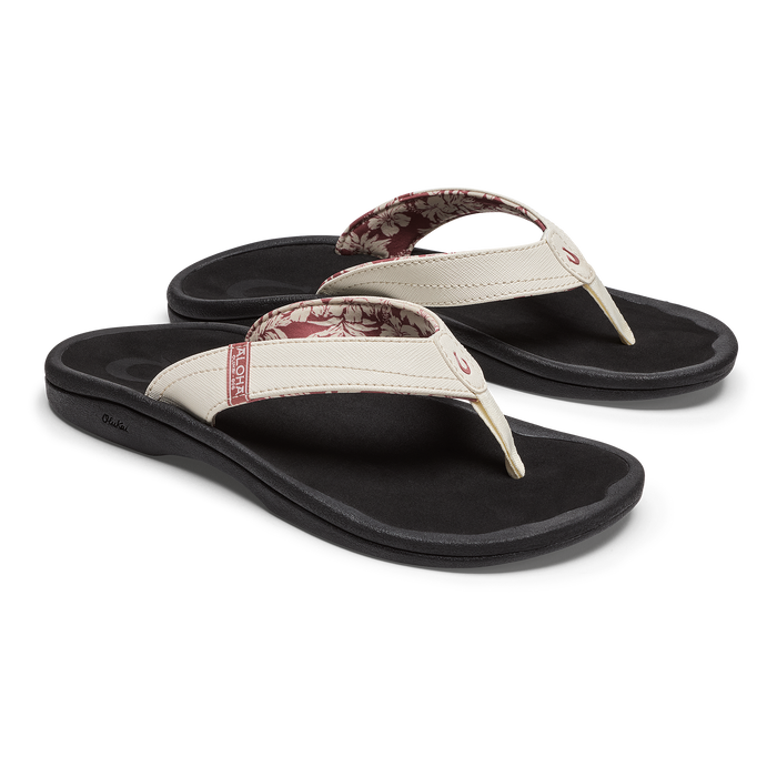 Pair of black flip-flops with white sand straps and patterned inner soles, shown from above at an angle.