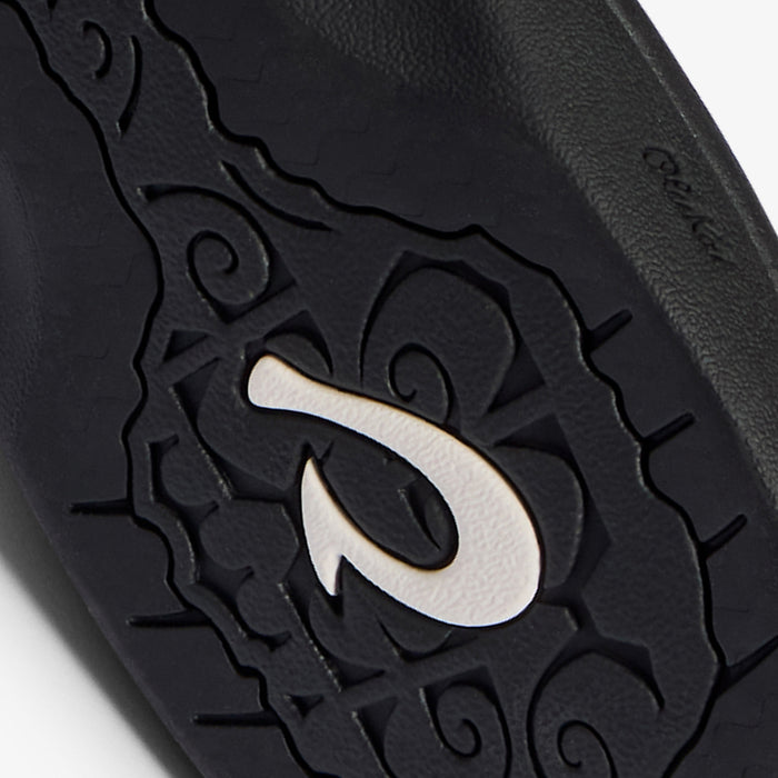 Black sandal with embossed decorative pattern and white sand inlay detail on upper surface.