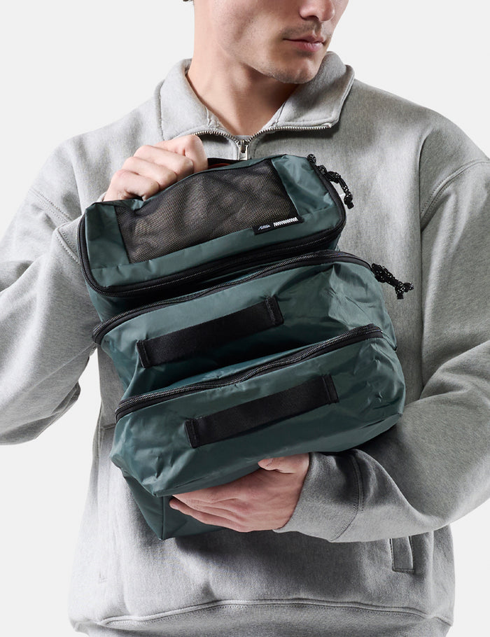Person holding a green travel packing cube set against a neutral background