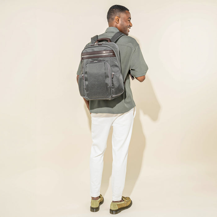 rear lifestyle view of a male model wearing the vintage grey travelpro platinum elite business laptop backpack 27l, showing the bag's fit against a casual outfit and highlighting the dark brown leather trim and padded shoulder straps.