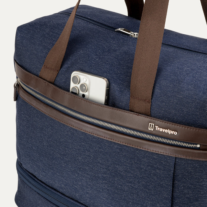 close-up of the front exterior of the true navy travelpro platinum elite weekender bag, showing a smartphone tucked into the quickslip pocket with premium chrome hardware and leather trim.