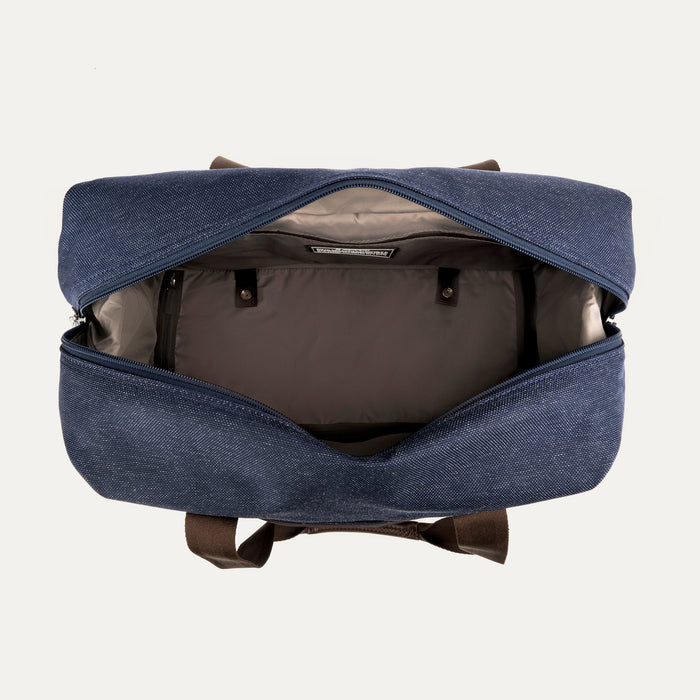 top-down view looking into the open drop-bottom compartment of the true navy travelpro platinum elite weekender bag, showing the interior organization, tan lining, and snap-button compression straps.