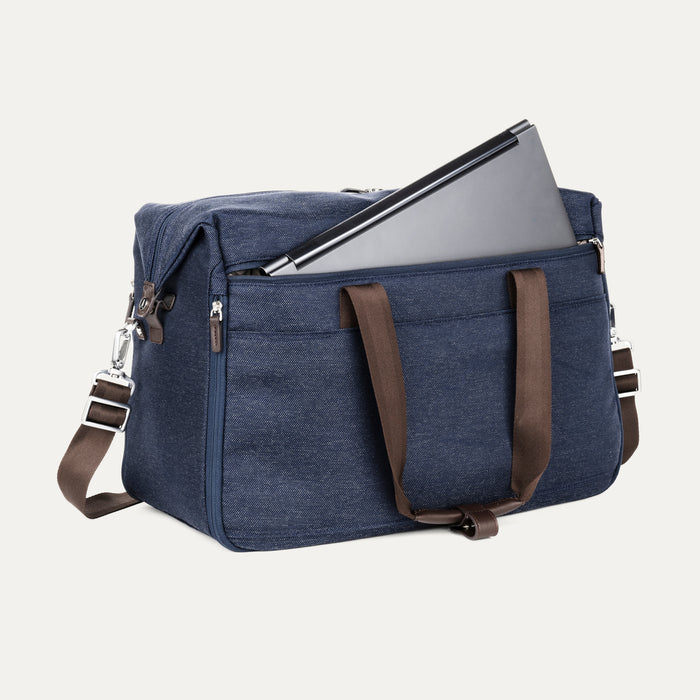 Front angle view of the Travelpro Platinum Elite Soft Duffel in True Navy, showing brown leather handles, front zip pocket with laptop partially inserted, and detachable shoulder strap against a white background.