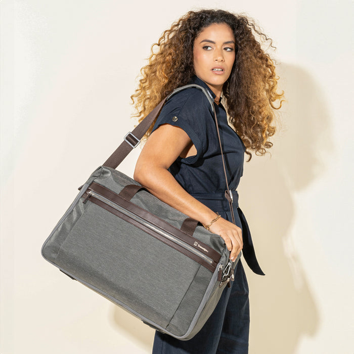 Lifestyle view of the Travelpro Platinum Elite Soft Duffel in Vintage Grey, carried by a model using the adjustable shoulder strap, showing brown leather trim, front zip pocket, and silver hardware against a light background.