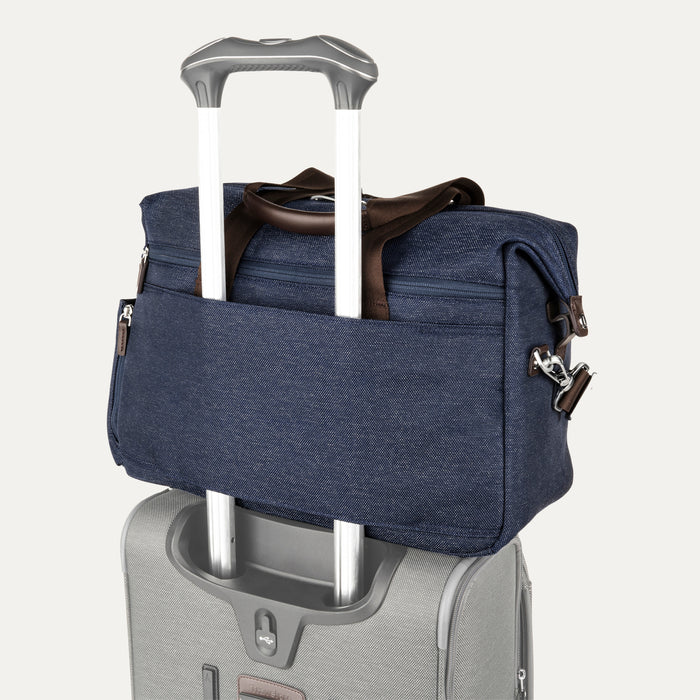 a true navy travelpro platinum elite underseat tote stacked on top of a silver rolling suitcase, with its integrated rear trolley strap securely slid over the luggage extension handle for easy transport.