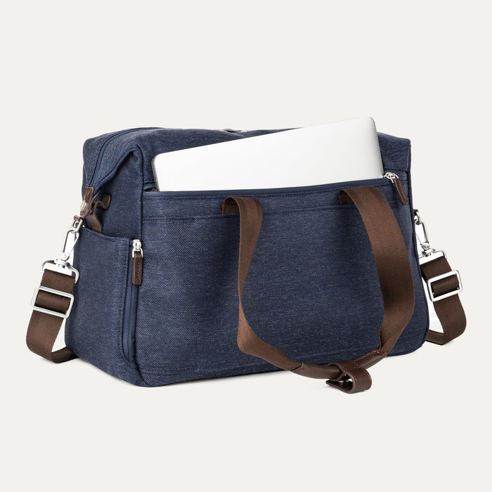 a true navy travelpro platinum elite underseat tote shown with a white laptop being inserted into the internal padded electronics sleeve, highlighting the bag's organization and protection for tech devices.