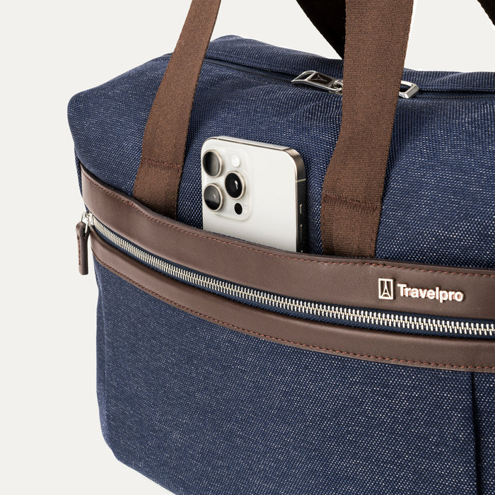 close-up of the front exterior of the true navy travelpro platinum elite underseat tote, showing a smartphone tucked into the quickslip pocket with brown leather trim and the travelpro logo.