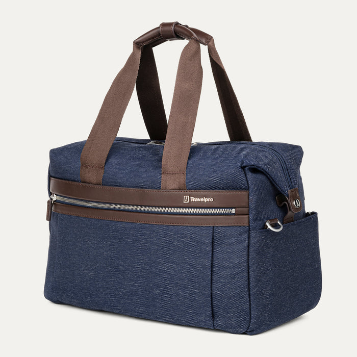 a three-quarter perspective view of the true navy travelpro platinum elite underseat tote, highlighting the textured blue fabric, brown leather trim, front zippered pocket, and side accessory pocket.