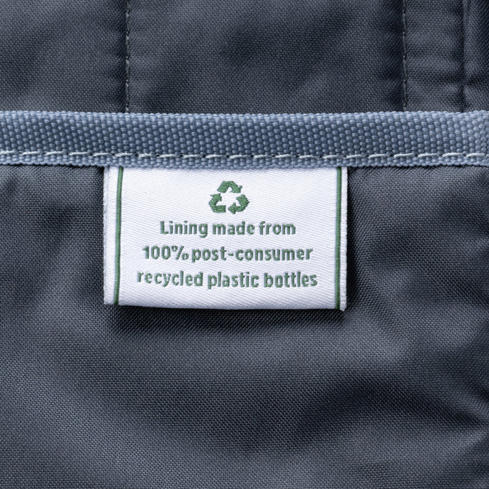close-up of the interior lining of the true navy travelpro platinum elite underseat tote, showing a white fabric label with a green recycling symbol that reads "lining made from 100% post-consumer recycled plastic bottles."