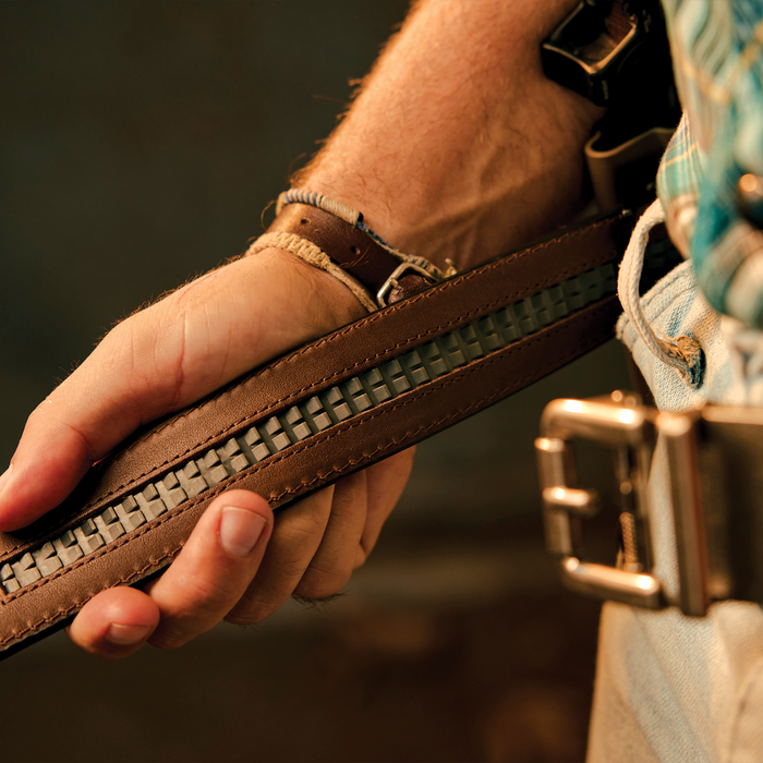 A man showcases the inside ratcheting track of a brown kore essentials ranch series gun belt