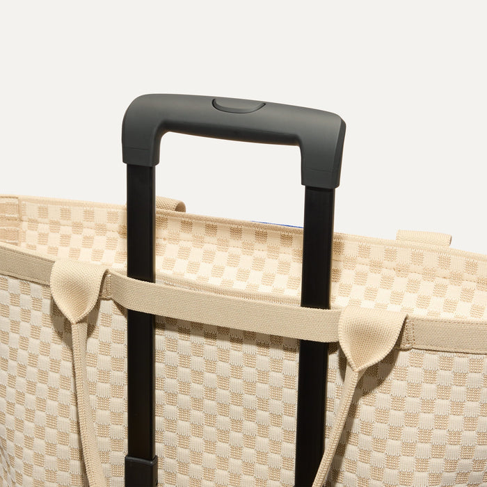 The Zip Travel Tote in  Parchment Basketweave, shown attached to a rolling suitcase using the wrap-around band.