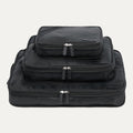 A set of three black Travelpro packing cubes in sizes XL, L, and M, stacked inside each other with zipper closures visible.