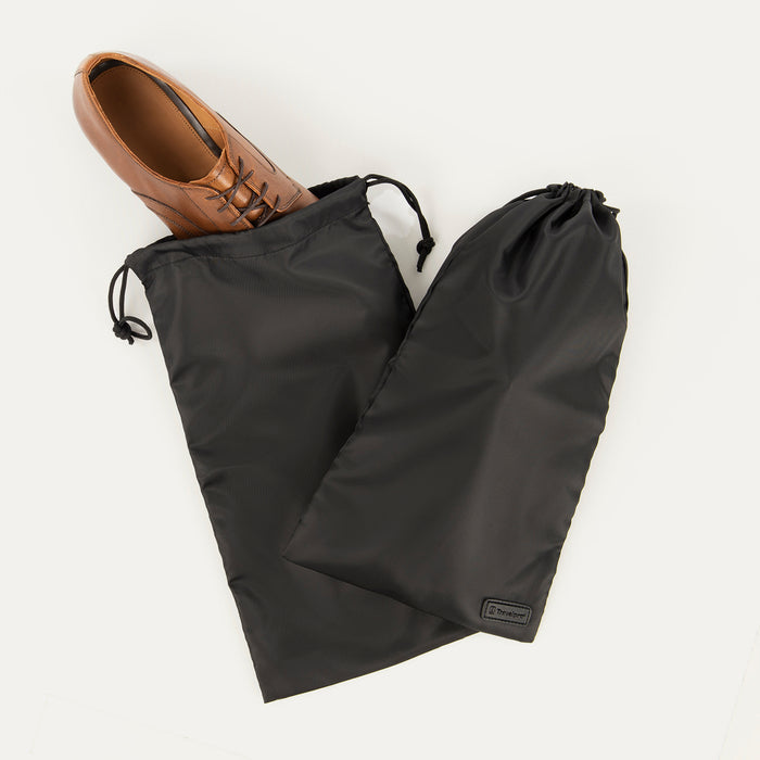 A pair of black Travelpro Essentials shoe bags with a single shoe placed in one of the bags, on a white background.