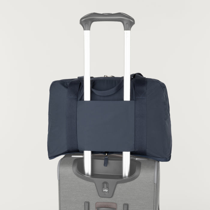 Rear view of the Travelpro Essentials SparePack Foldable Duffel 2.0 in Navy, demonstrating the integrated stacking strap used to secure the duffel onto the extension handle of a rolling suitcase for hands-free carrying.
