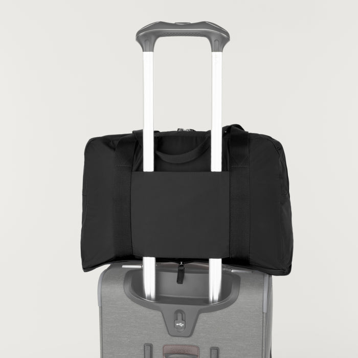 Rear view of the Travelpro Essentials SparePack Foldable Duffel 2.0 in Black, demonstrating the integrated stacking strap used to secure the duffel onto the extension handle of a rolling suitcase for hands-free carrying.