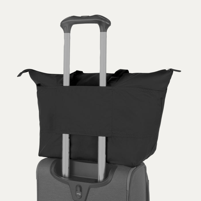 Rear view of the Travelpro Essentials SparePack Foldable Tote 2.0 in Black, demonstrating the integrated stacking strap used to secure the tote onto the extension handle of a rolling suitcase for hands-free carrying.