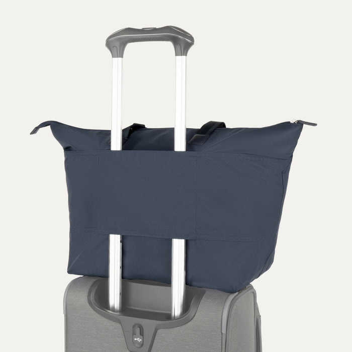 Rear view of the Travelpro Essentials SparePack Foldable Tote 2.0 in Navy, demonstrating the integrated stacking strap used to secure the tote onto the extension handle of a rolling suitcase for hands-free carrying.