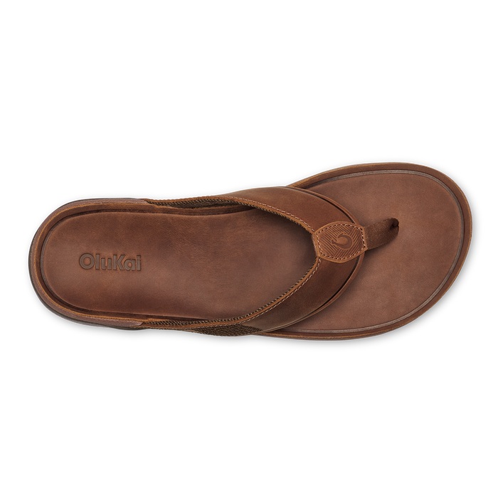 Brown leather thong sandal with circular embellished strap detail and OluKai branding on insole, shown from above.