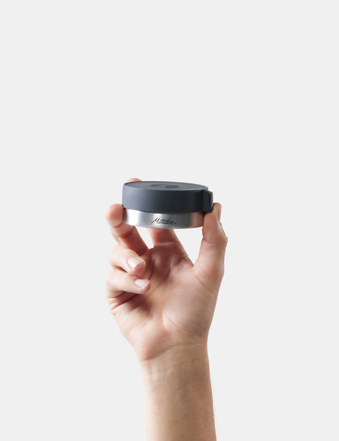 Hand holding a black and silver container with 'Matador' branding against a white background
