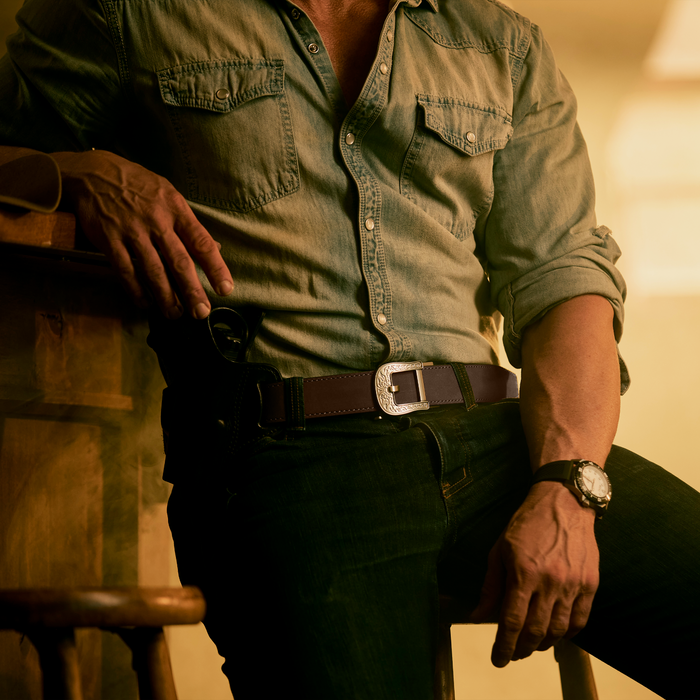 A man sits at a bar wearing all denim and a Kore Essentials coffee buffalo leather EDC gun belt.
