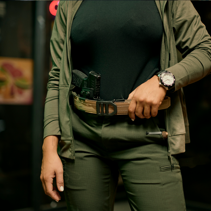 A woman wears a 1.5" Kore Essentials USA Desert Tiger Stripe EDC gun belt with a firearm holstered at the appendix position.