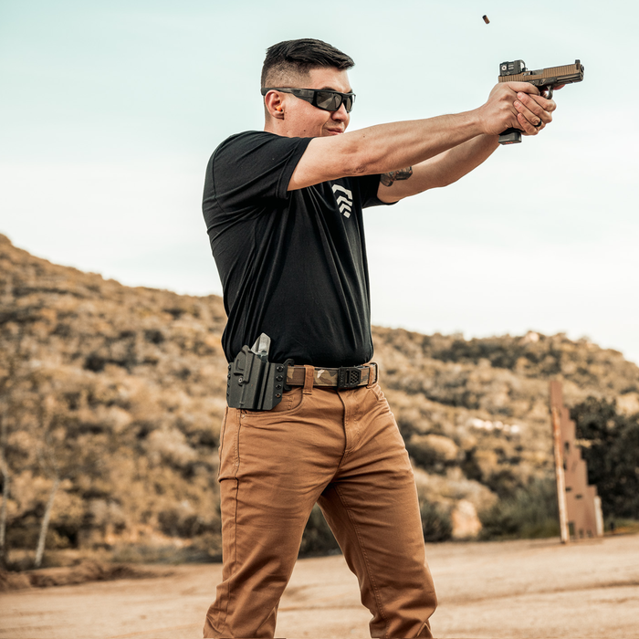 A man wearing a 1.5" Kore Essentials EDC gun belt draws his firearm and takes aim at a shooting range.