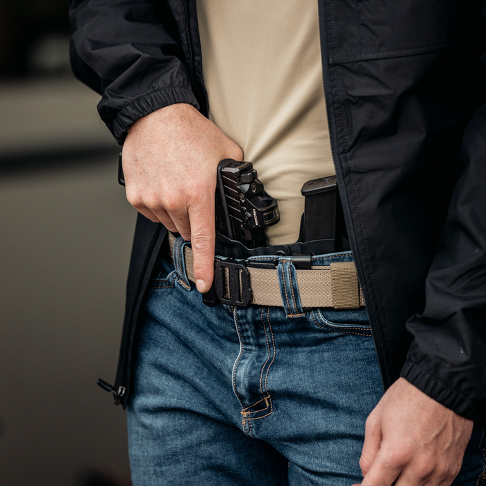 Close-up shot of a man wearing a tan 499 edc gun belt from Kore Essentials while he's carrying a firearm at the appendix position.