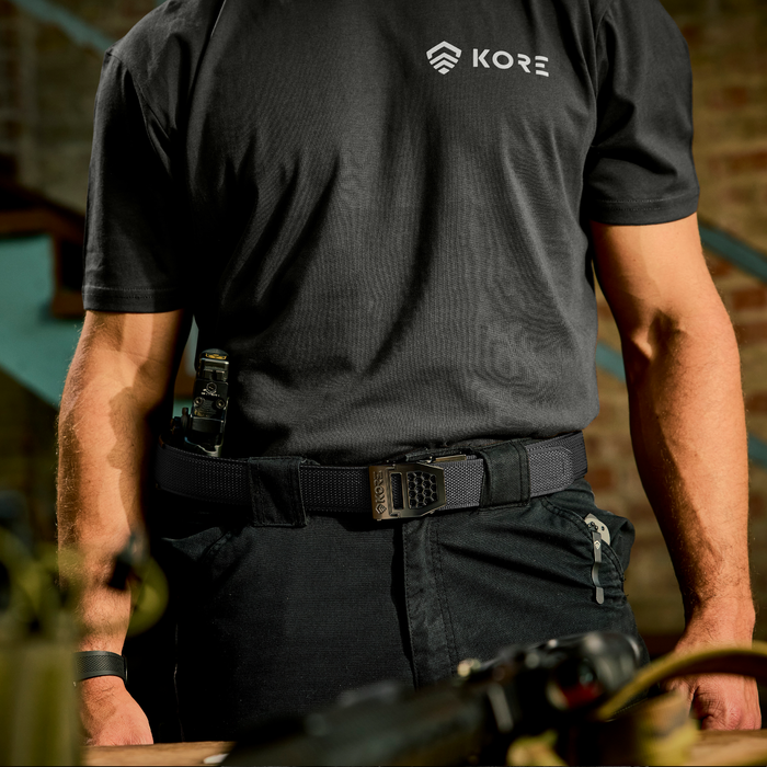 A person stands wearing a Kore Essentials black tactical nylon EDC gun belt with a gunmetal X6 buckle.