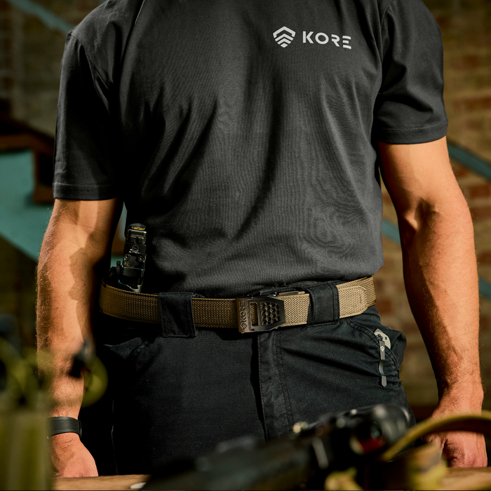 A person stands wearing a Kore Essentials USA 1.5" coyote tactical nylon gun belt for EDC and concealed carry.